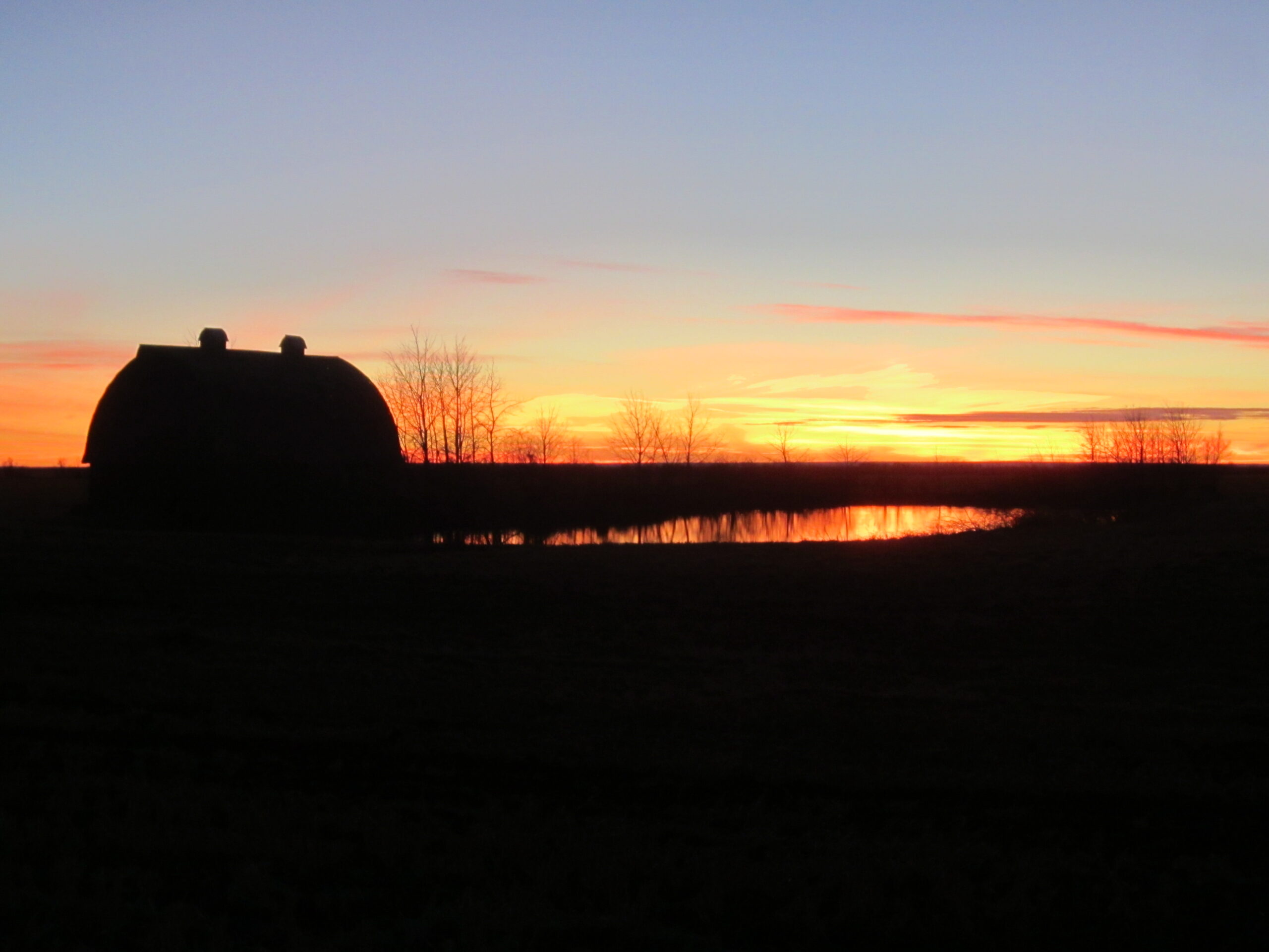 Barn at sunset beside a pond.