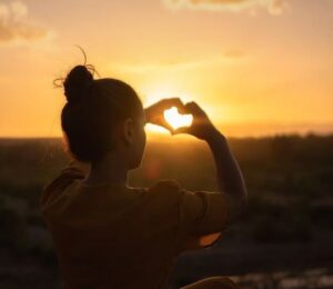 Girl holding hands up to sun and holding them like a heart.